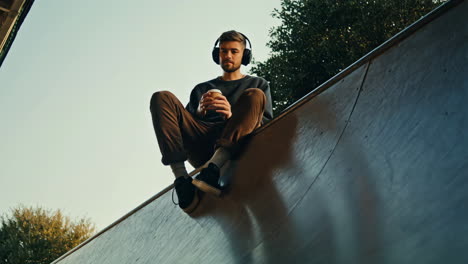 young man with headphones drinking coffee outdoors