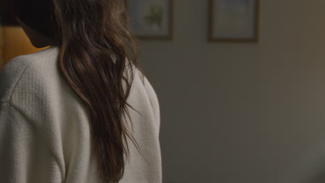 woman spending evening at home carrying hot drink and mobile phone sitting on sofa and opening laptop