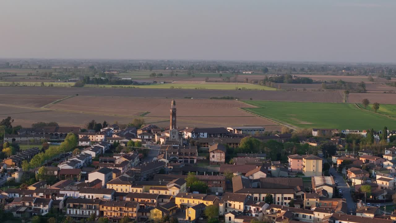 Spinadesco a Cremona, Lombardia, Italia, con torre campanaria e tessuto urbano compatto, campi coltivati nella Pianura Padana, con rete stradale locale visibile e traffico leggero, ripresa aerea statica in allontanamento.