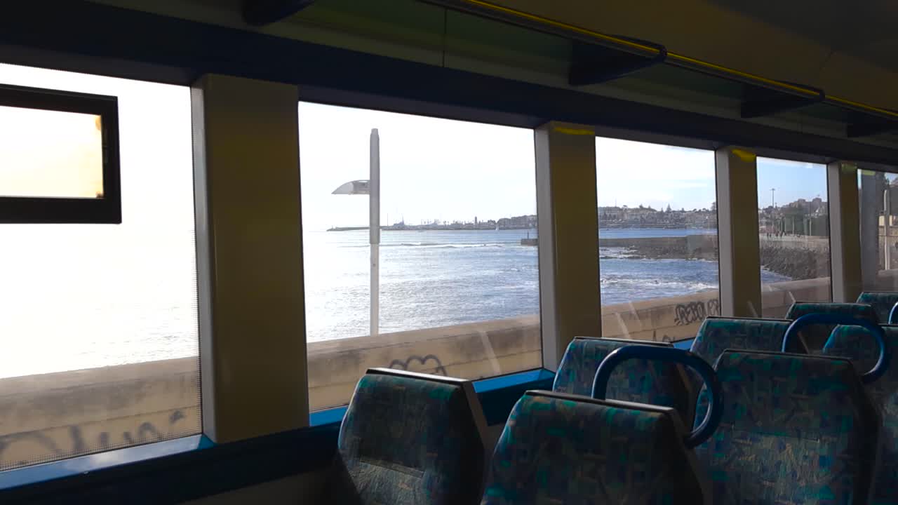 Vista interna di un treno portoghese in movimento con sedili vuoti mentre la luce del sole rivela la costa rocciosa attraverso i finestrini durante un viaggio da Lisbona a Cascais