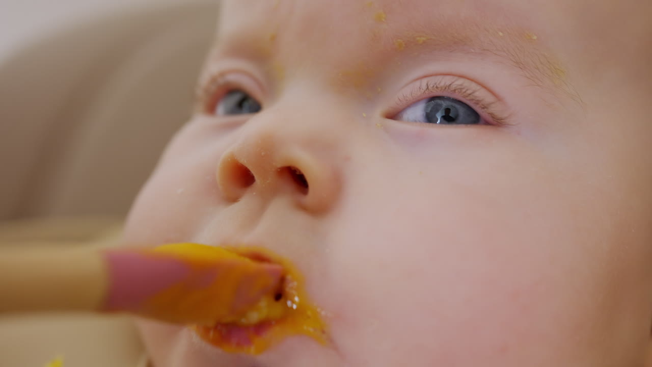 スプーンで離乳食を与えられている赤ちゃんのクローズアップ。顔の細部と穏やかな表情が見える。