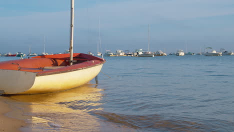 small boat on seashore moving by calm waves with yachts in background in arcachon, france