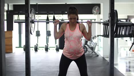 imágenes de una modelo embarazada haciendo sentadillas en un gimnasio tratando de mantenerse en forma en su cuarto trimestre.