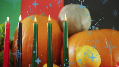 Animation-of-blue-stars-over-kwanzaa-candles-and-pumpkins