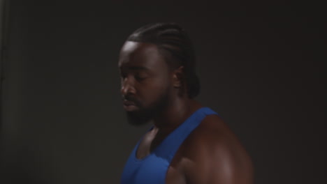 close up portrait of serious male boxer wearing vest walking away from camera training for sports event against black studio background