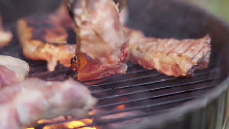 slow motion of tongs flipping sizzling meat on fiery and smokey bbq grill