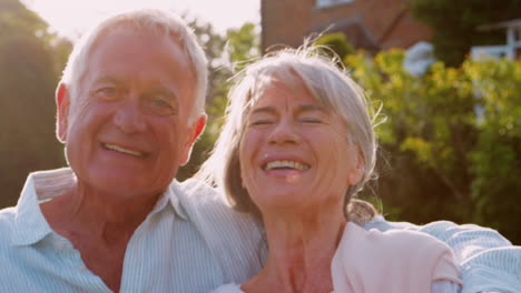 Portrait-Of-Senior-Couple-Sitting-On-Garden-Bench-In-Evening