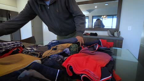 a casually dressed man arranges school clothes on a table