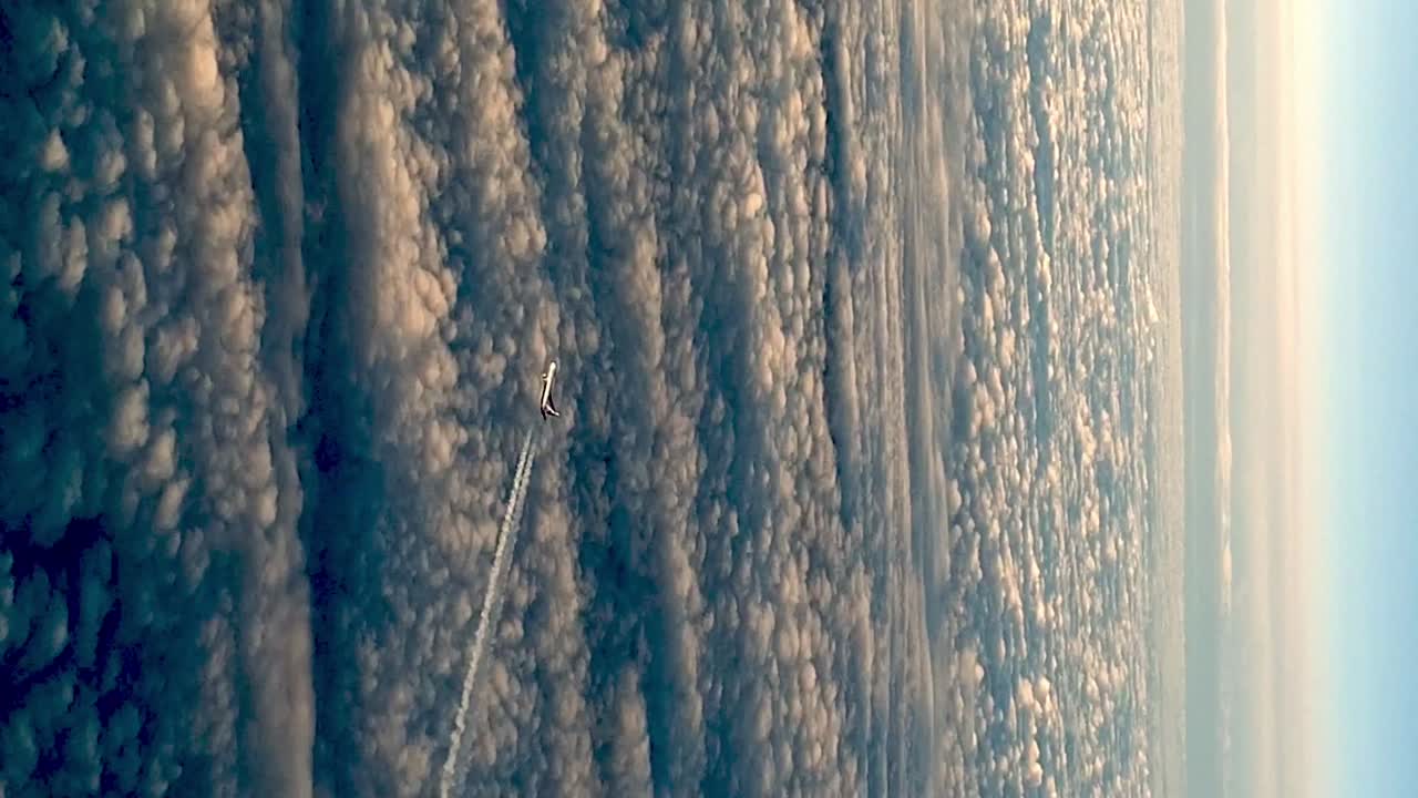 Flying airplane above clouds leaving condensation vapor air trail in blue sky
