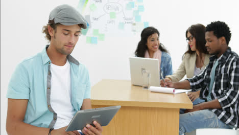 hombre sonriente usa la tableta mientras los colegas trabajan detrás de él