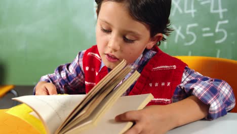 Schoolboy-reading-book-in-classroom-at-school