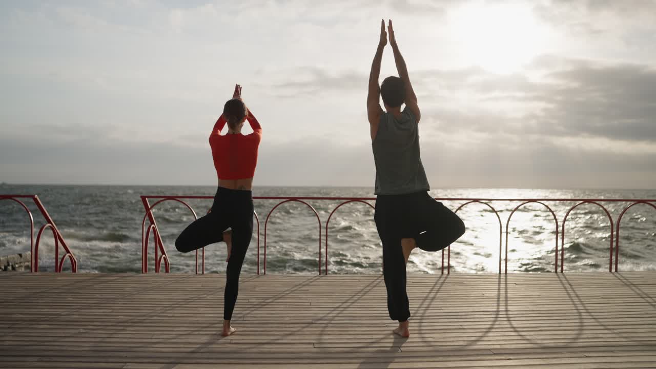 una pareja practicando yoga en un muelle de la playa