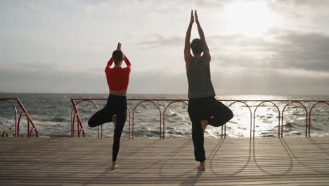 couple practicing yoga on a beach pier