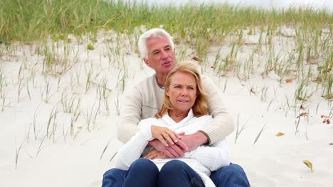 Smiling-retired-couple-sitting-on-the-beach