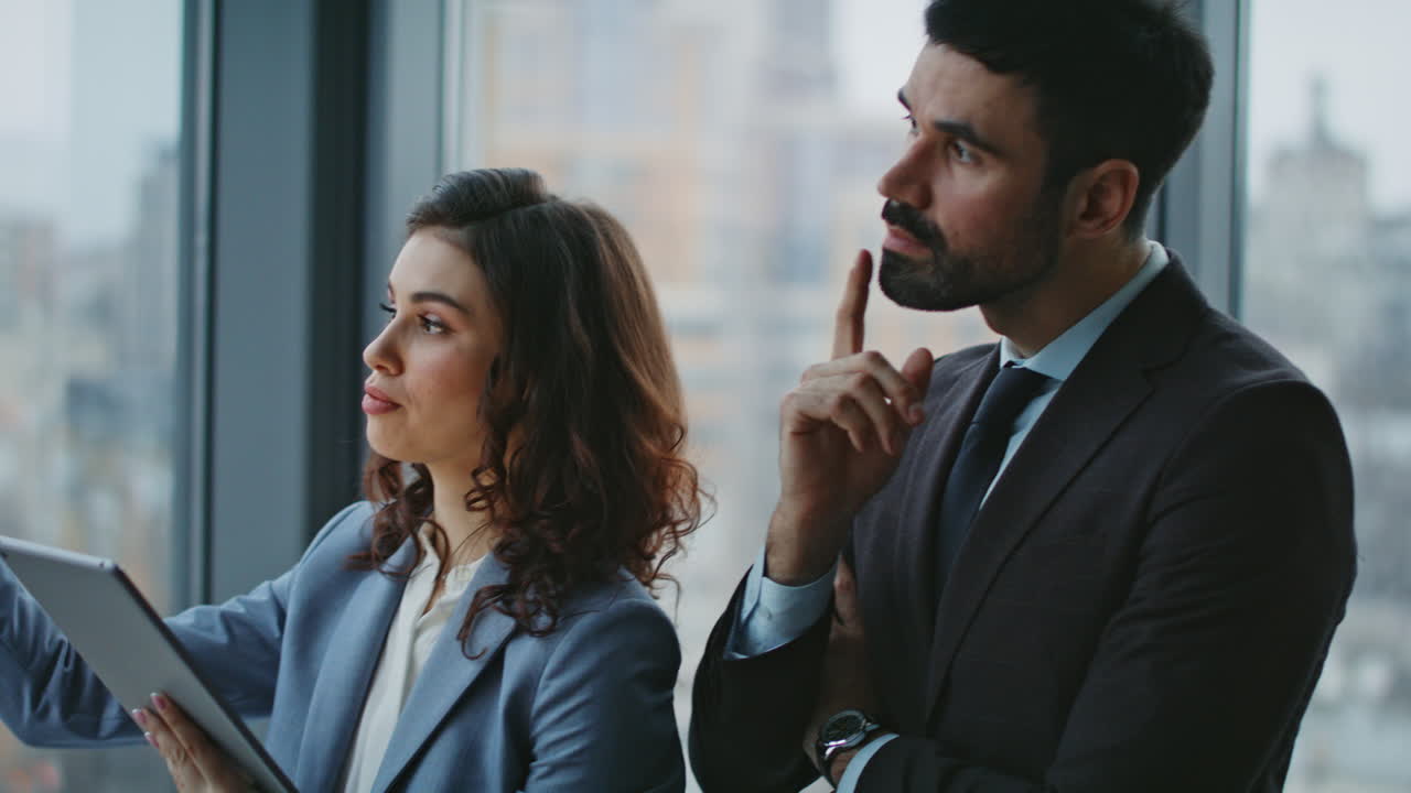 una mujer sonriente presentando un plan de trabajo al jefe de pie cerca de la ventana.