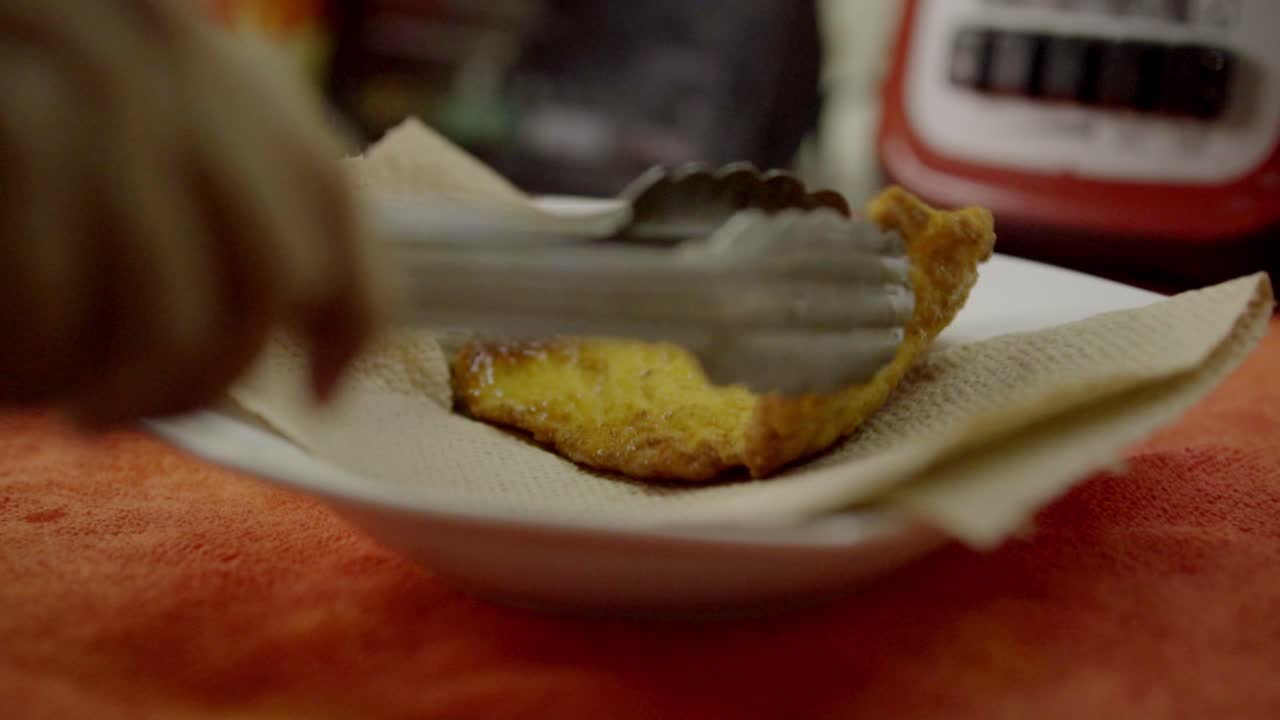 Pinze che sollevano dolci fritti su carta in cucina, ambiente caldo