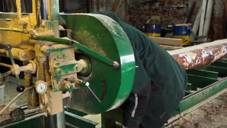 mechanic repairs dirty bandsaw machine in sawmill for log sawing into planks