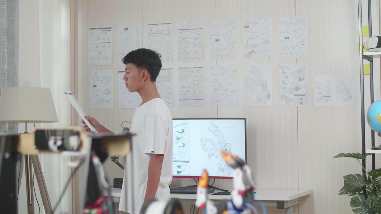 아시아 소년이 손에 든 그림을 보고, 생각하고, 집에서 사이보그 손에 대해 일하면서 돌아다니고 있습니다.