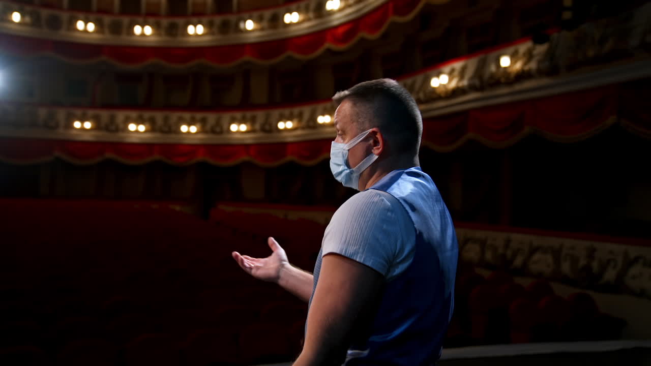 Actor on stage. Man in medical mask is talking to empty auditorium. Speaker in protective mask during the rehearsal. Rear view.