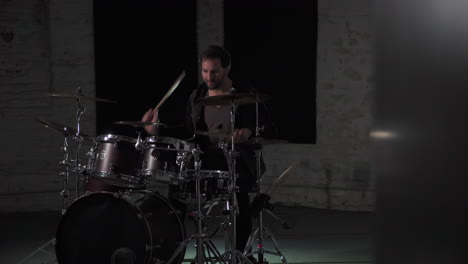 a young man plays on his favorite drumset in a dark room of his basement.