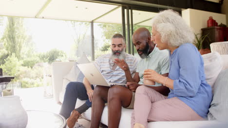 senior friends sitting on couch, using laptop and enjoying coffee together