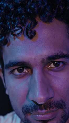 contemplative young man with curly hair experiencing emotional shifts, bathed in vibrant purple and blue lighting during intimate studio portrait session