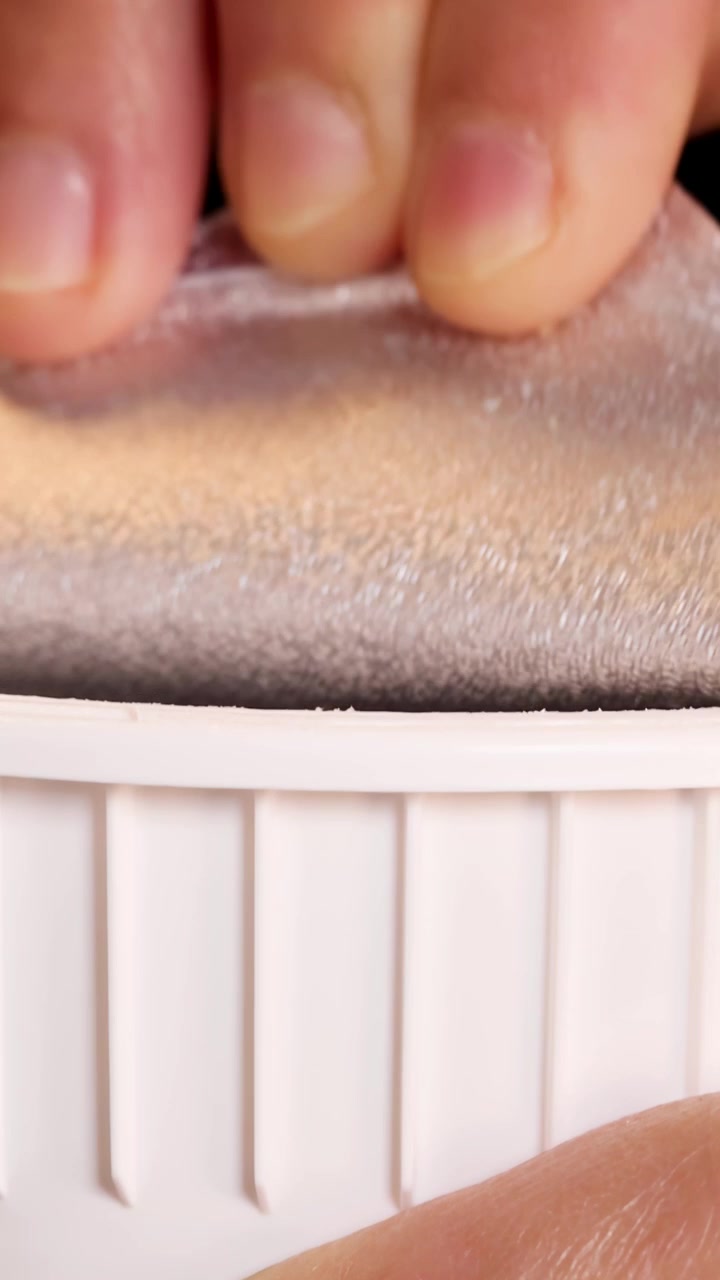 Primo piano di una mano che stacca il coperchio di alluminio da una tazza di noodle istantanei bianca su uno sfondo scuro.