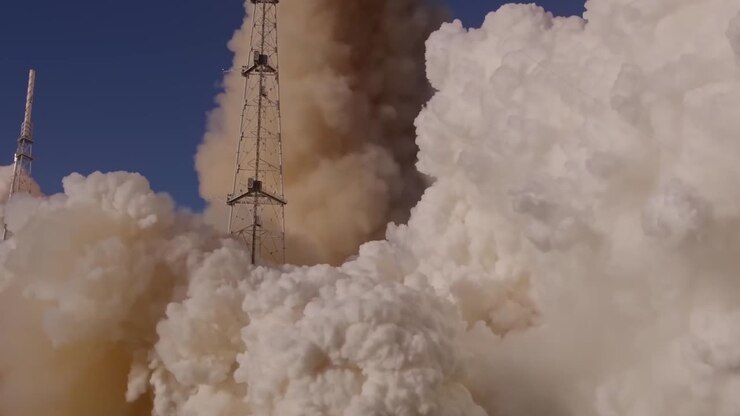 A massive rocket engine ignites at the launchpad creating thick clouds of smoke and fire during a daytime liftoff