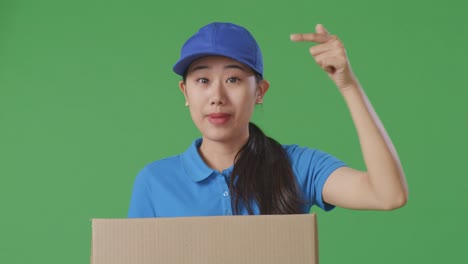 close up of asian female courier in blue uniform smiling and talking to camera while delivering a carton on green screen background in the studio