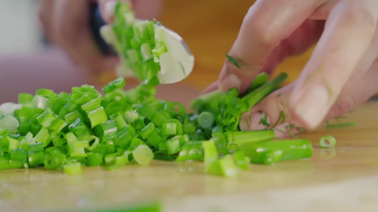 A close up of a female cook chopping a bunch of fresh green onions on a wooden cutting board