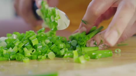 A-close-up-of-a-female-cook-chopping-a-bunch-of-fresh-green-onions-on-a-wooden-cutting-board