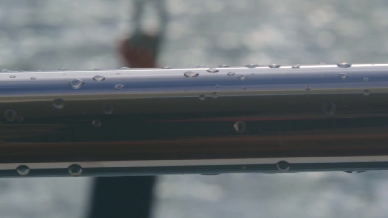 Pulling focus from a stainless bar on a boat with water drops on it, to a buoy out in the water.