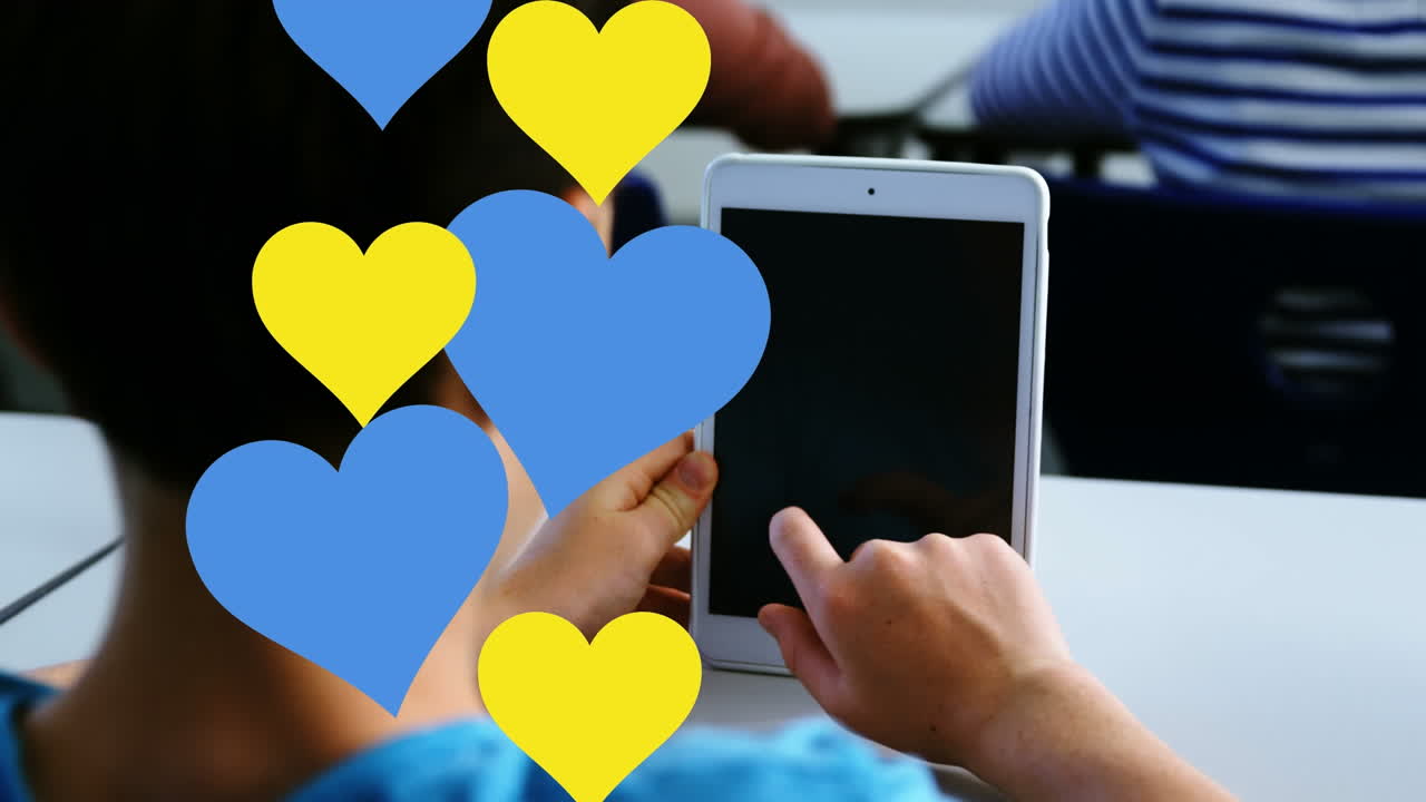 학교에서 디지털 태블릿을 사용하는 백인 소년의 뒷면에 여러 개의 파란색과 빨간색 심장 아이콘이 있습니다.