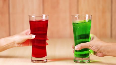 two hands exchanging red and green drinks