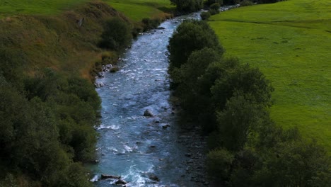 Drone-flying-over-green-meadow-of-Furka-pass-and-river-stream-flowing-in-summer-season,-Switzerland