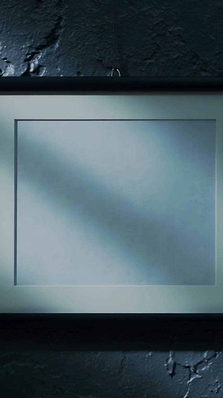 Vertical video: Shifting light casting soft shadow on framed panel on dim wall with hook and cracks