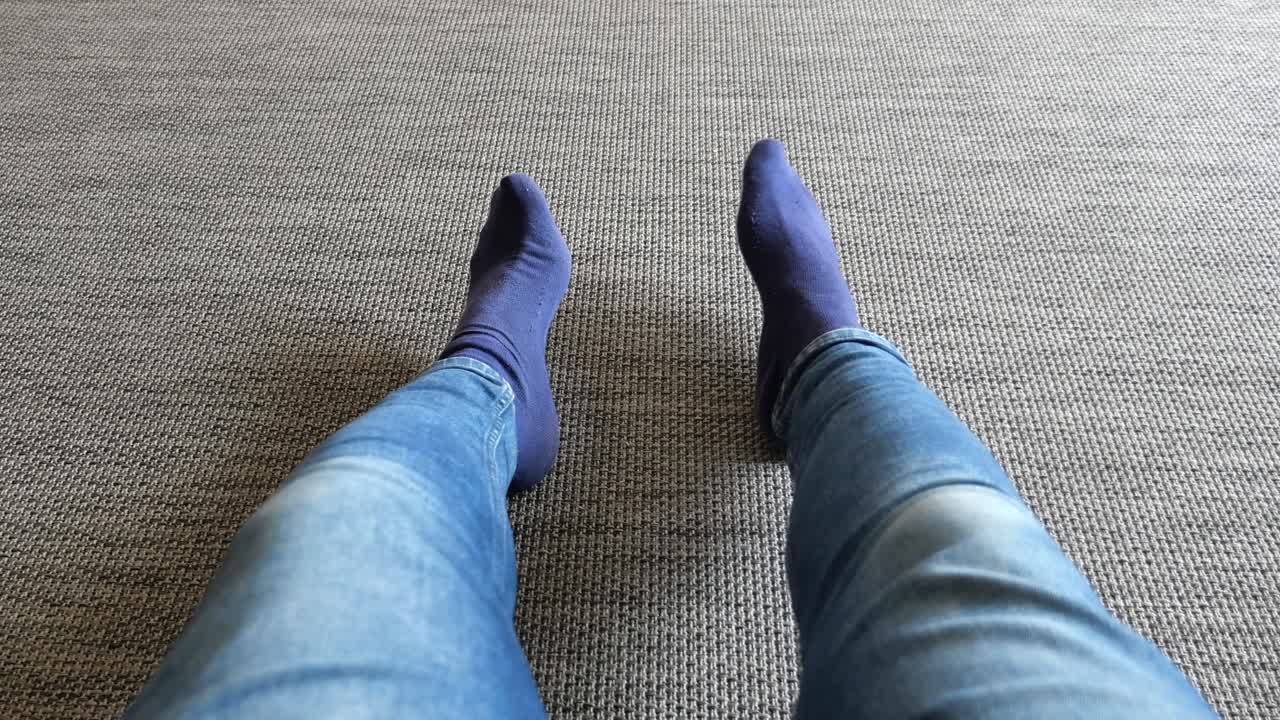 persona con pantalones vaqueros azules y calcetines azules sentada en un piso de alfombra