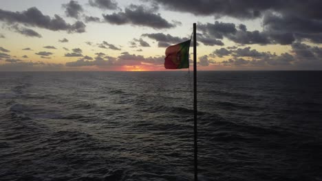 static shot of portuguese flag in the wind, strong wind moving flag by the atlantic ocean during sunset