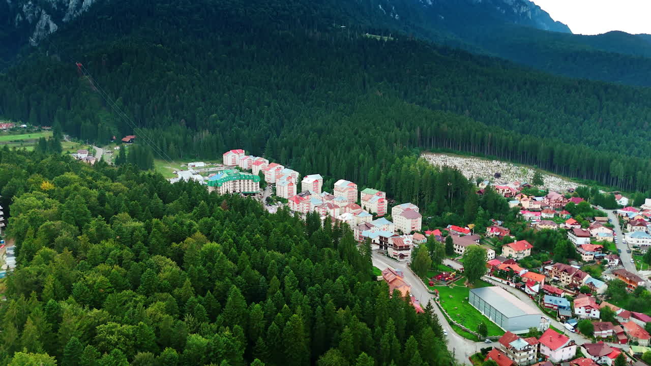 City of Busteni located in the pine tree woods covering the Carpathian Mountains in Romania. Drone flight over the lush forests around the residential area