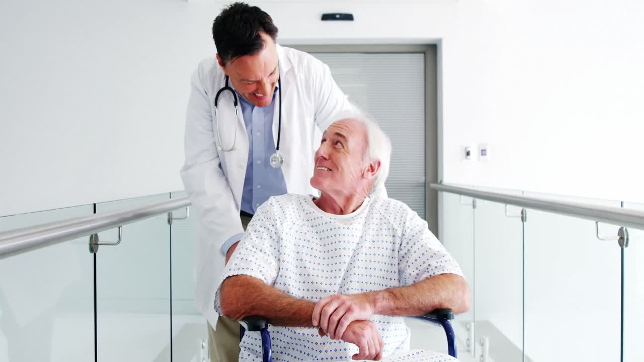 médico sosteniendo a un paciente mayor en silla de ruedas en el pasillo