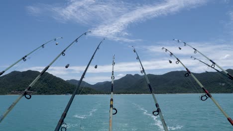 遠くの山に面したボートの後ろから釣り竿がぶら下がっています