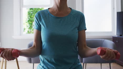 Caucasian-senior-woman-exercising-with-dumbbells-while-sitting-on-the-gym-ball-at-home