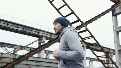 side view of a young sportsman in grey hoodie jogging in a old factory ruins on a cloudy morning