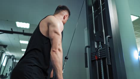 muscular man trains on the simulator in fitness center. strong athlete pull bar with rope and weights on fitness machine indoors.