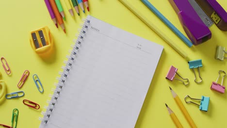 Video-of-school-supplies-and-notebooks,-paper-clips,-pens-over-yellow-background