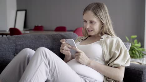 happy pregnant woman typing on smartphone