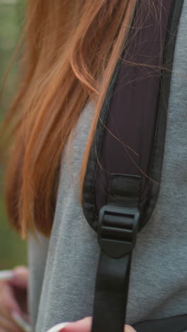 primer plano de una mujer joven con suéter gris, al aire libre, con cabello rojo vibrante y luz natural suave en un entorno forestal, centrado en el área del hombro