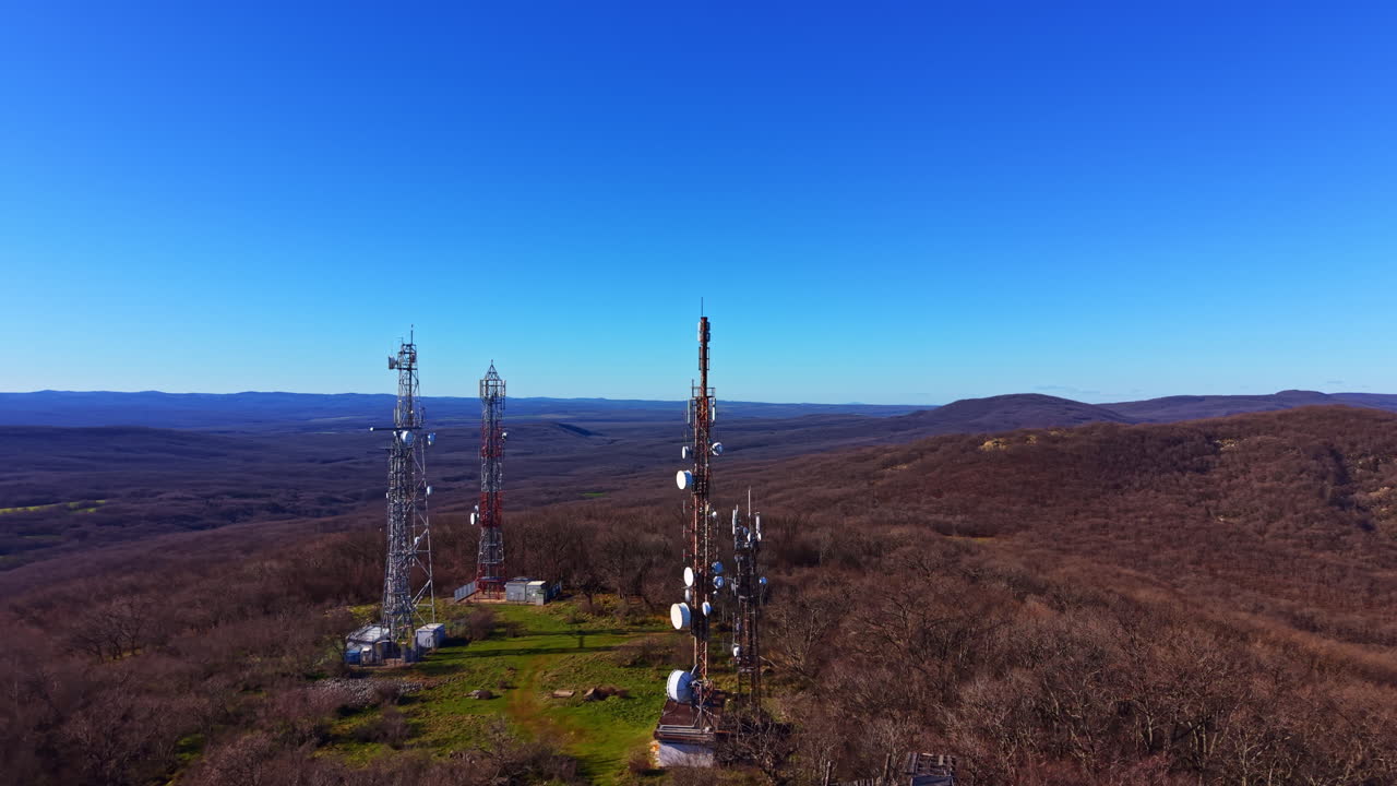 Telecommunication towers on a hilltop with clear skies and distant mountains in the background during daytime