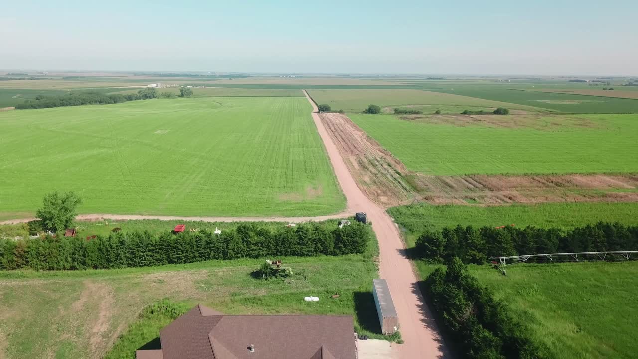 vista aérea de drones siguiendo un camino de grava que sale de un patio de granja a lo largo de un campo de soja