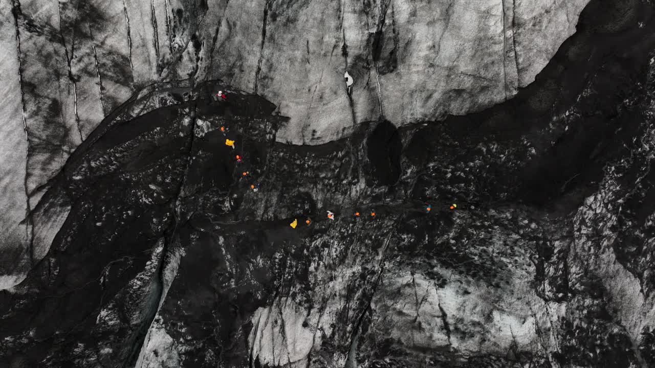 Drone shot of a group of hikers exploring the rugged surface of Sólheimajökull glacier in Iceland, showcasing deep crevasses and jagged ice.